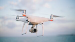 White quadcopter camera drone hovering in flight against a pale sky